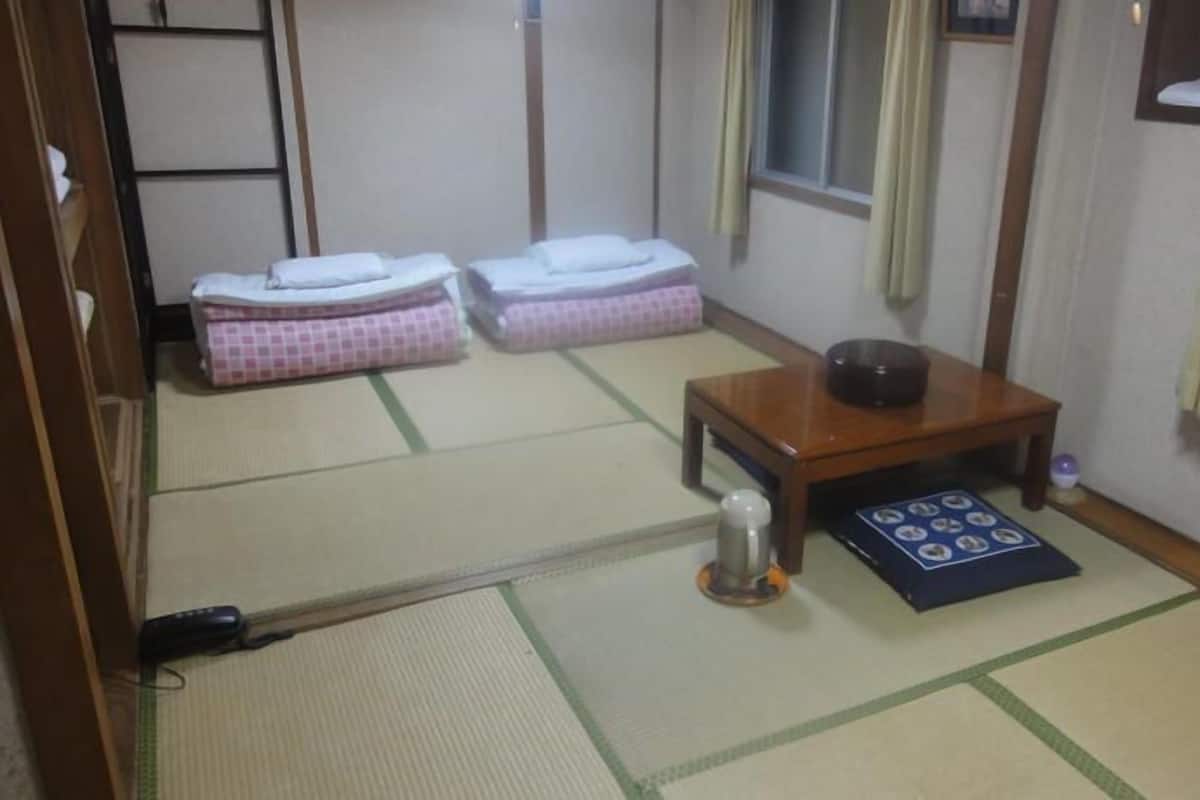 A traditional Japanese room with tatami flooring, a futon bed, a small wooden table with a bowl, and a shoji screen.