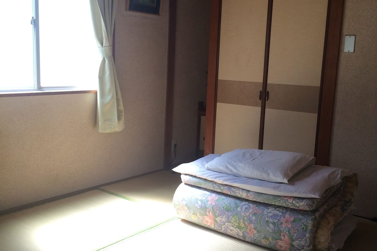 A room with tatami flooring, a futon bed, a sliding door, and a window with a curtain.