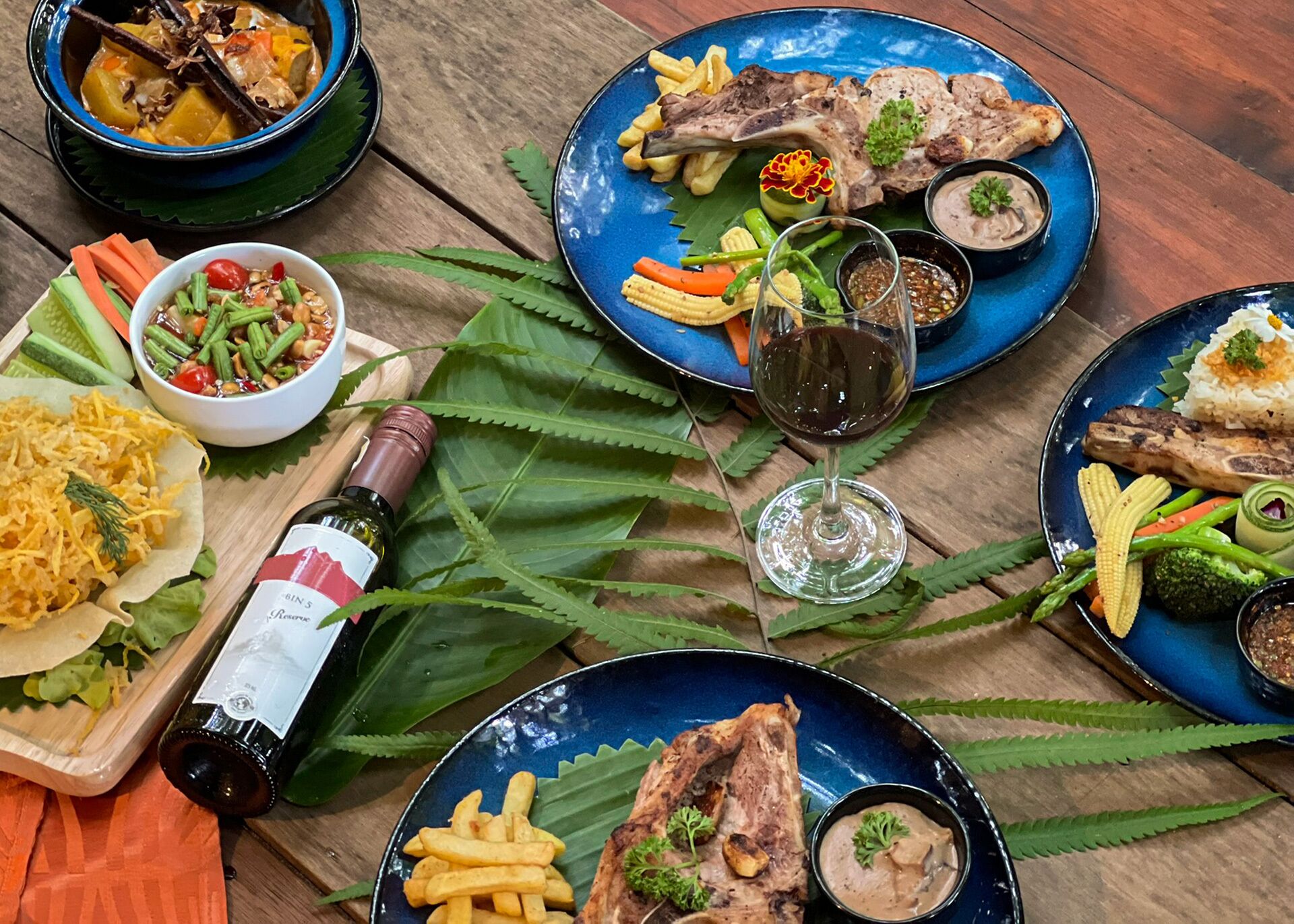 A table set with various dishes, including steak, fries, and a salad, along with a bottle of wine and a glass.