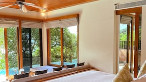 Un dormitorio con una cama grande, un ventilador de techo y vistas a una piscina a través de amplios ventanales.
