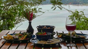 Una mesa servida con varios platos y una copa de vino tinto, con vistas a un paisaje que incluye una masa de agua y montañas.