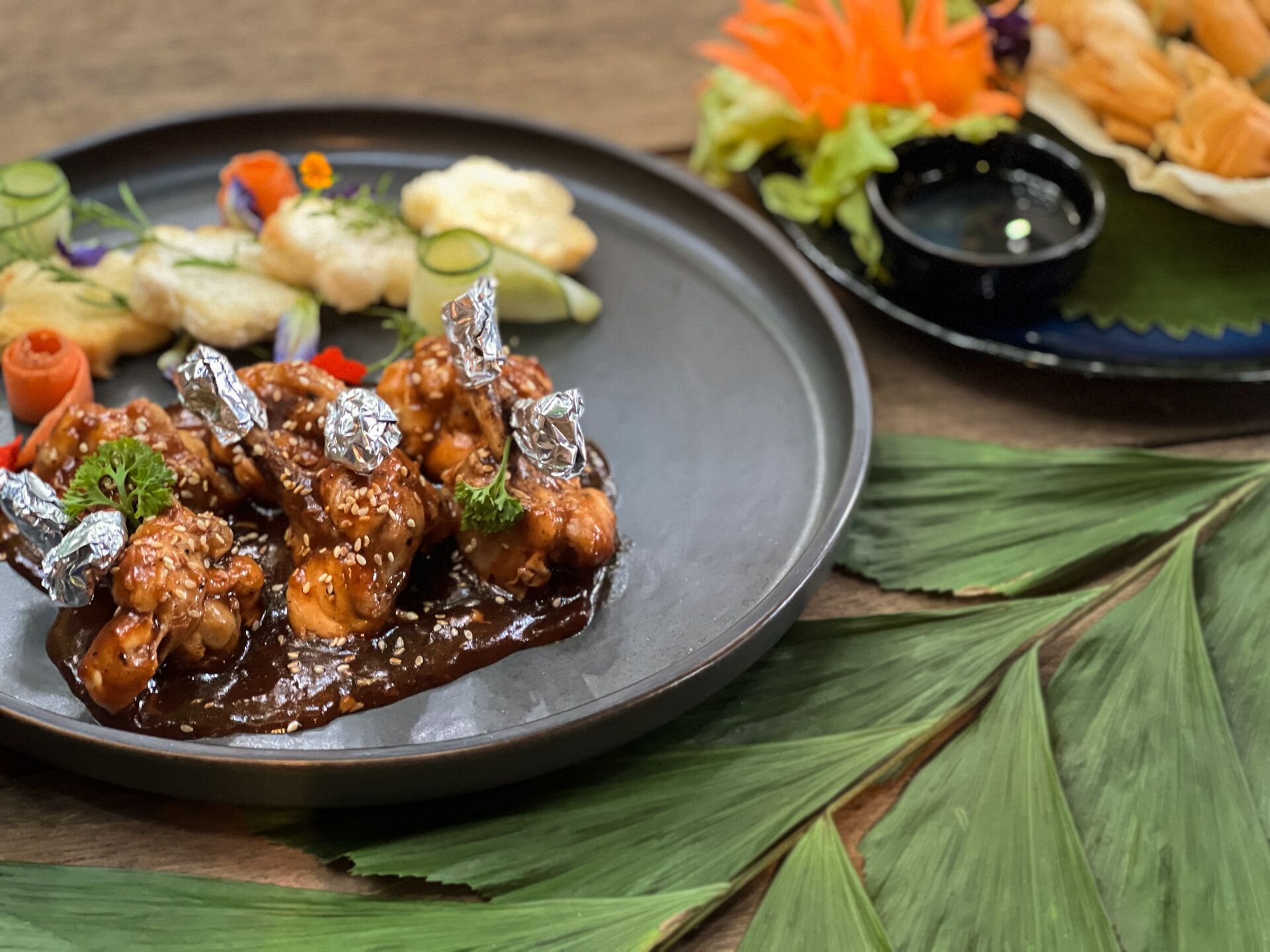 A plate of food with a variety of items including a dish with a dark sauce, vegetables, and a small bowl of sauce.