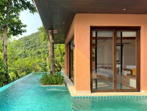 Uma casa moderna com porta de vidro que dá para um quarto, rodeada por uma piscina e vegetação exuberante.