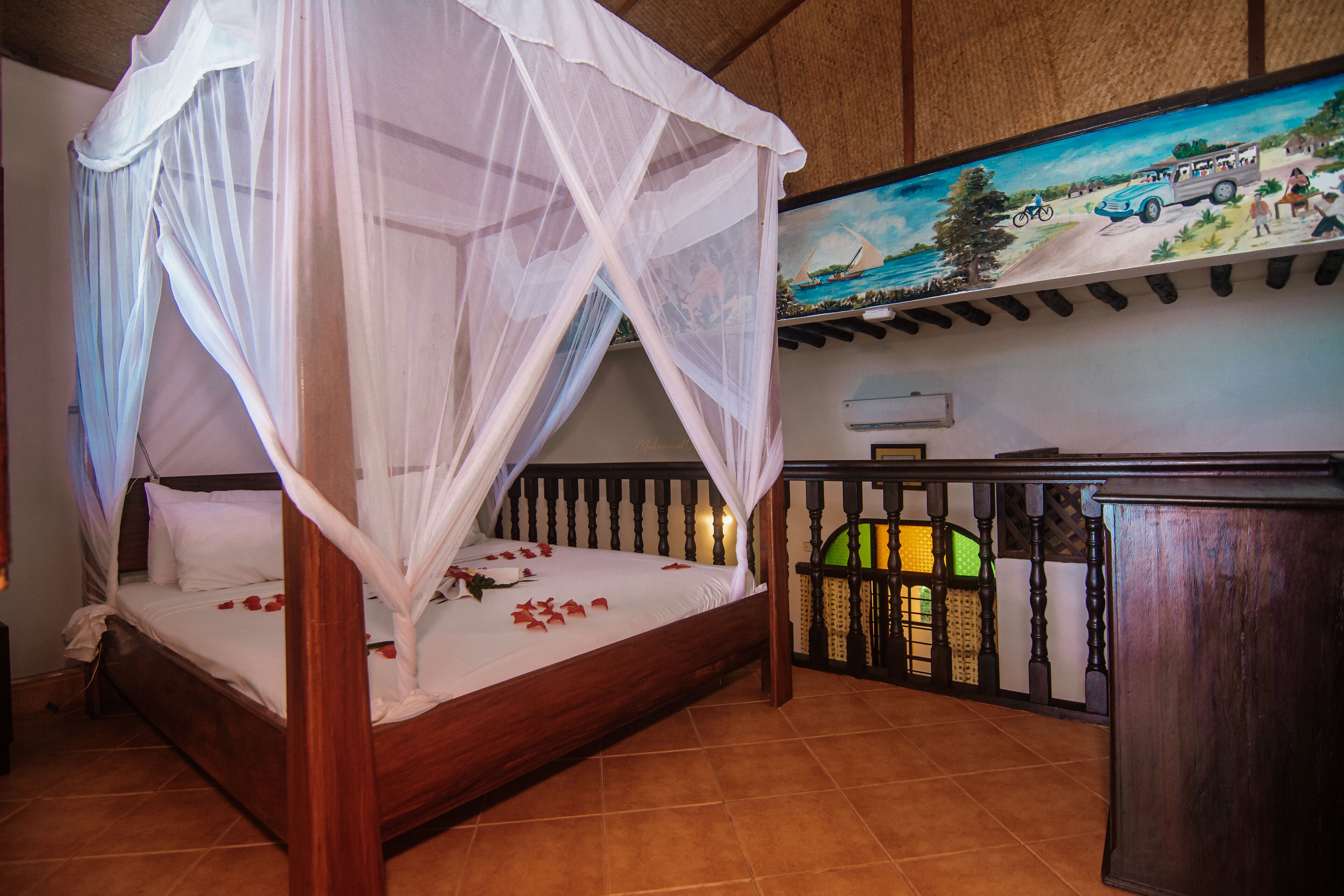 A bed with a canopy, a painting on the wall, and a wooden desk.