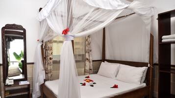 A neatly made bed with a canopy, a bedside telephone, and a mirror on a wooden nightstand.