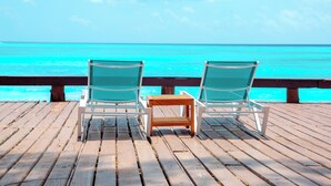 Deux fauteuils confortables sont placés face à une terrasse en bois, offrant une vue sur l’océan.