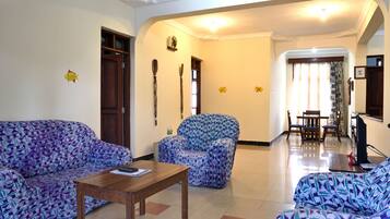 A living room with patterned sofas, a wooden coffee table, and a dining area with a TV.