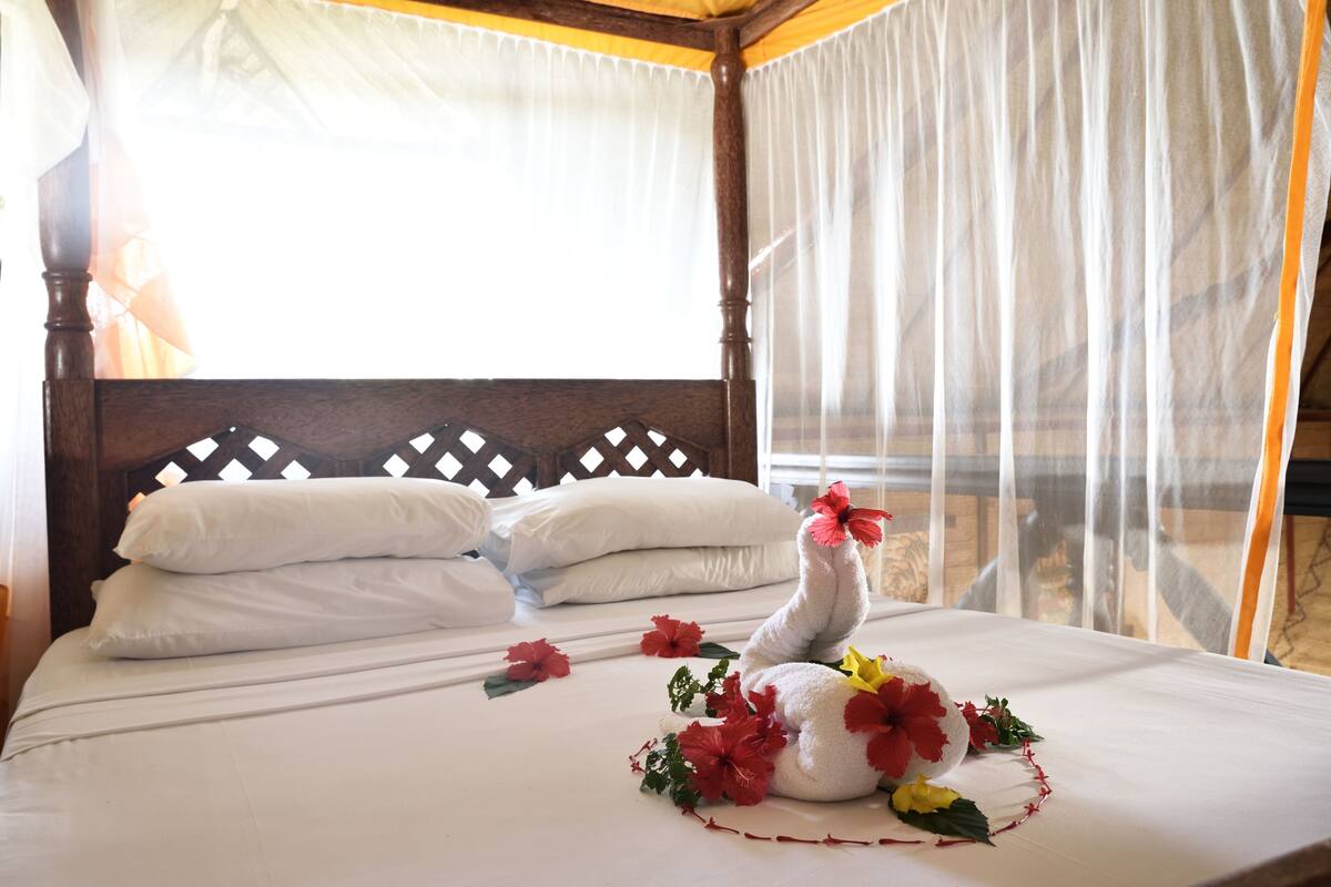 Un llit amb roba de llenceria blanca, un capçal de fusta i una peça decorativa d'un cigne amb flors vermelles.