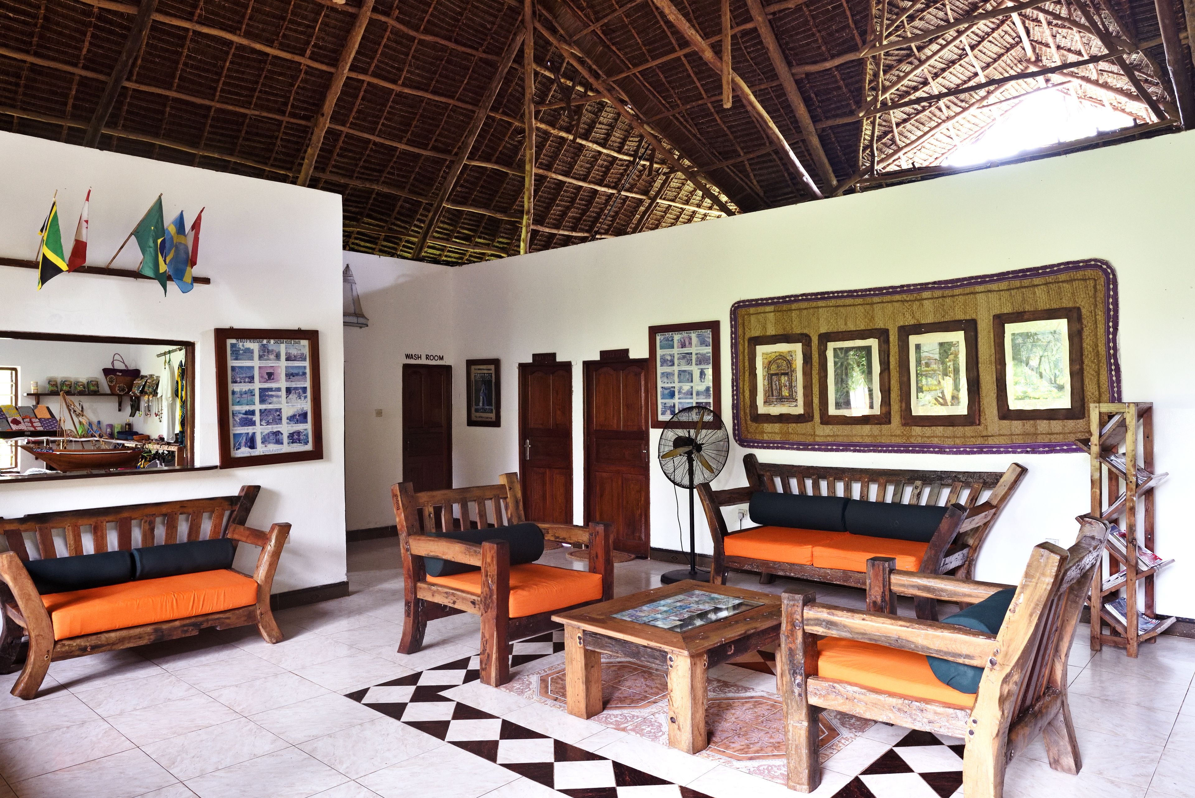 A spacious lobby with wooden furniture, a checkered floor, and a high ceiling with a thatched roof.