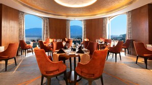 A dining area with round tables, orange chairs, and large windows offering a view of a mountainous landscape. - Radisson Blu Plaza Hotel Mysore (Mysore)