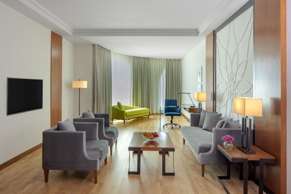 Habitación de hotel con zona de estar que incluye dos sofás, una mesita de centro y un televisor.