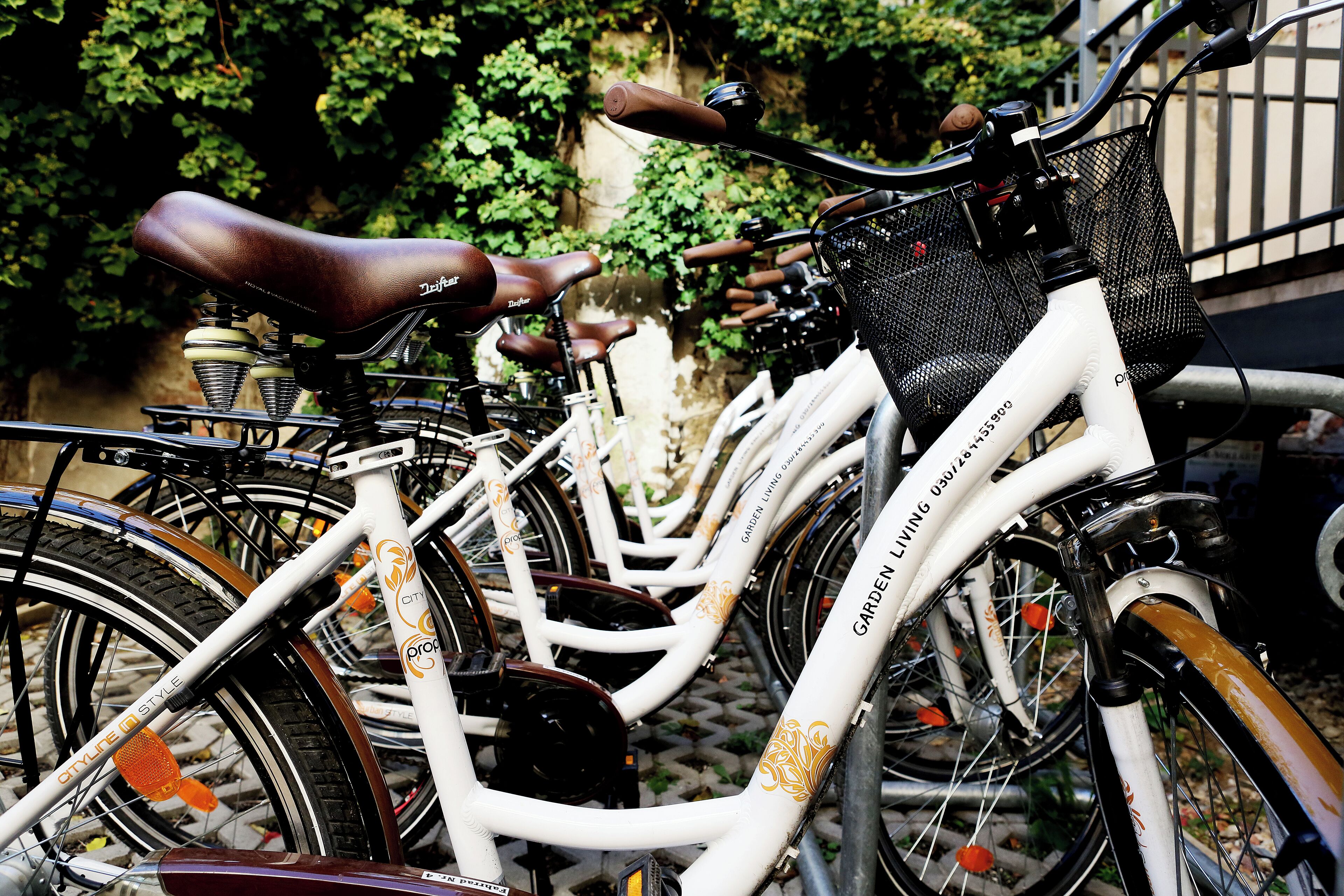 Een witte fiets met 'CITYLITE STYLE' en 'GARDEN LIVING' branding, geparkeerd op een geplaveid pad met begroeiing op de achtergrond.