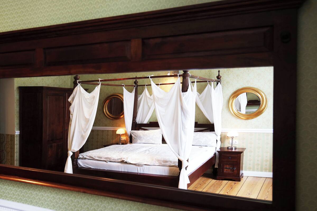 Un dormitorio con cama con dosel, un espejo grande y una mesita de noche.