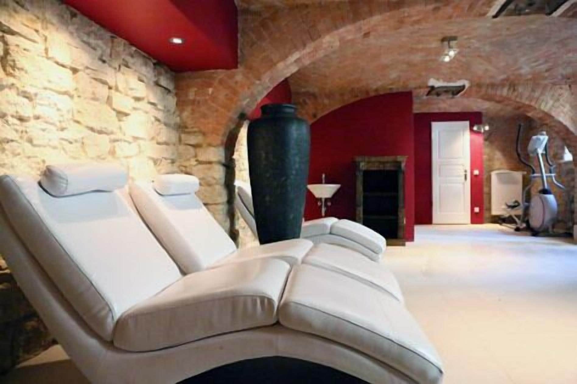 A spa room with a massage chair, stone walls, a fireplace, and a door leading to another room.