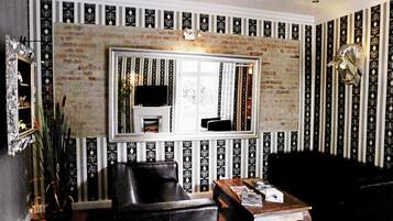 A room with a brick wall, a large mirror, a black leather chair, a wooden coffee table, and striped wallpaper.