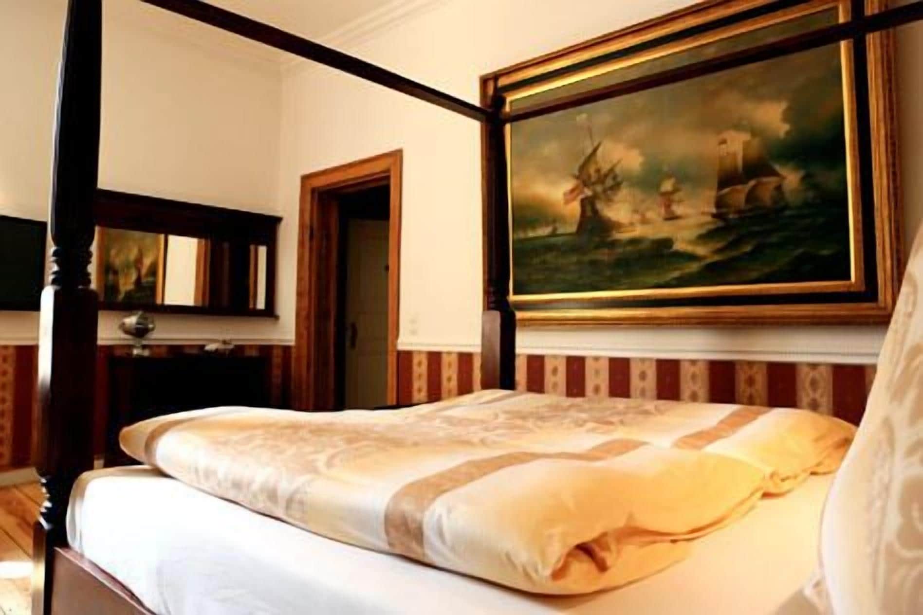 Ein Hotelzimmer mit einem Himmelbett, einem Gemälde darüber und einem Spiegel an der Wand.