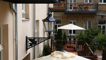 Uma varanda com mesa e cadeiras, um lanterna pendurada e vista para a fachada do edifício.