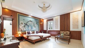 A spacious hotel room with a large bed, a wooden sofa, a desk, and a decorative wall mural. - Aris Resort (Phu Quoc)
