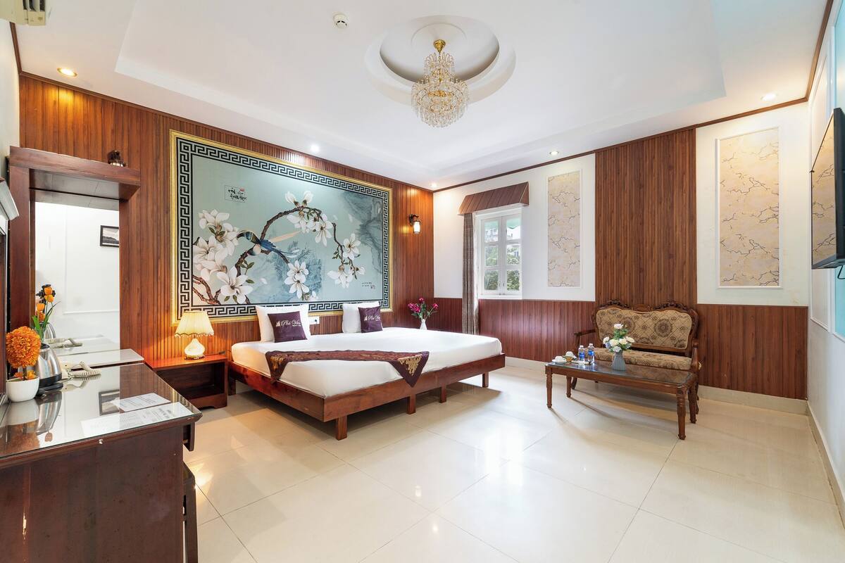 A spacious hotel room with a large bed, a wooden sofa, a desk, and a decorative wall mural.