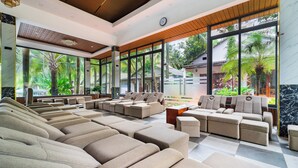 A modern waiting area with multiple seating options, large windows offering views of greenery, and a wooden ceiling. - Aris Resort (Phu Quoc)