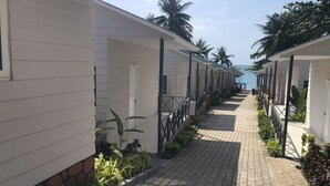 A row of white buildings with a paved walkway between them, lined with plants and palm trees in the background. - Aris Resort (Phu Quoc)
