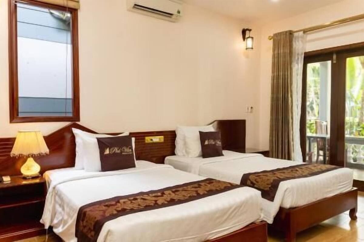 A hotel room with two beds, a nightstand with a lamp, a window with a view, and a balcony.
