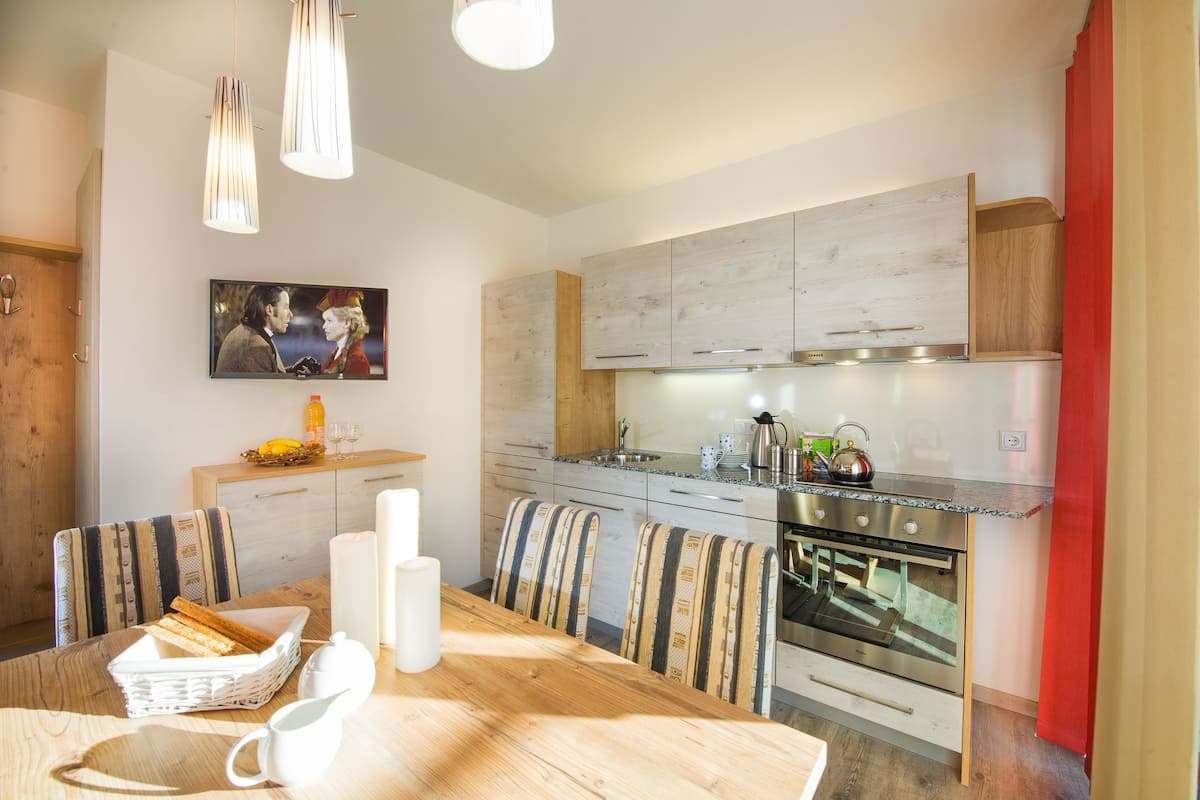 A modern kitchen with wooden cabinets, a built-in oven, and a dining area with striped chairs.