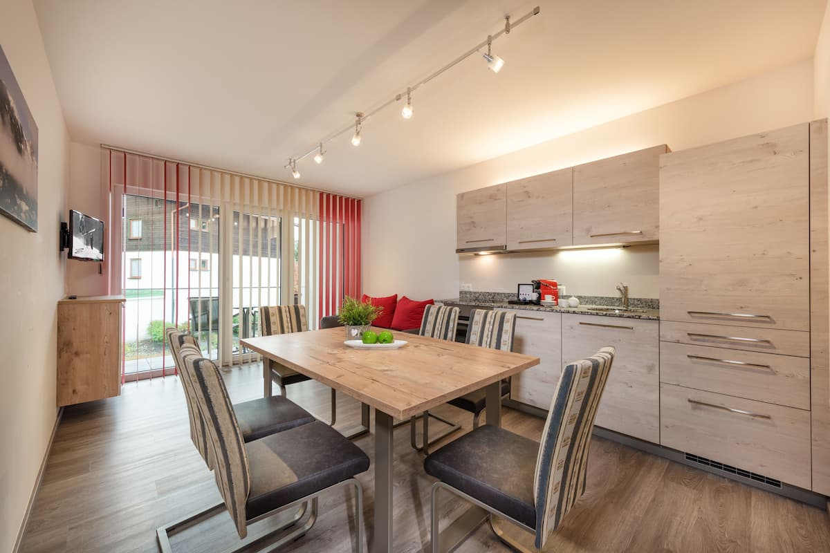 A modern kitchen with wooden cabinets, a dining table with chairs, and a sliding glass door leading to a balcony.