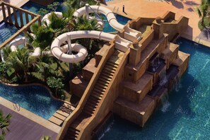 Un espace piscine doté de plusieurs toboggans et d’une terrasse en bois.