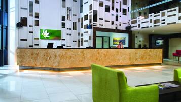 A modern reception area with a marble counter, green upholstered chairs, and a large screen displaying a flower.