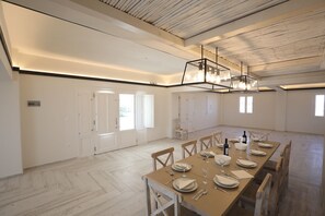 Ein geräumiger Essbereich mit einem langen Tisch, gedeckt für sechs Personen, Holzstühlen und einer modernen Chandelüster.