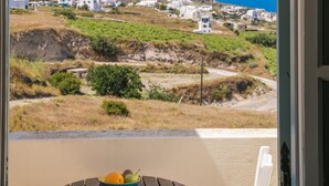 A view from a balcony with a table holding fruit, overlooking a coastal landscape with buildings and a hill.