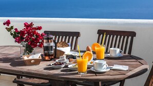 A wooden table with breakfast items, including orange juice, bread, and eggs, set on a balcony overlooking the sea.