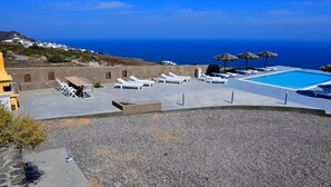 A rooftop pool area with lounge chairs and umbrellas, overlooking a coastal landscape.