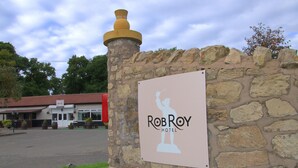 Señal del Hotel RobRoy, con un muro de piedra y un edificio al fondo.