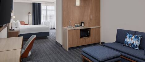 Ein Hotelzimmer mit Bett, Schreibtisch, Fernseher, Küchenzeile und einer Sitzecke.