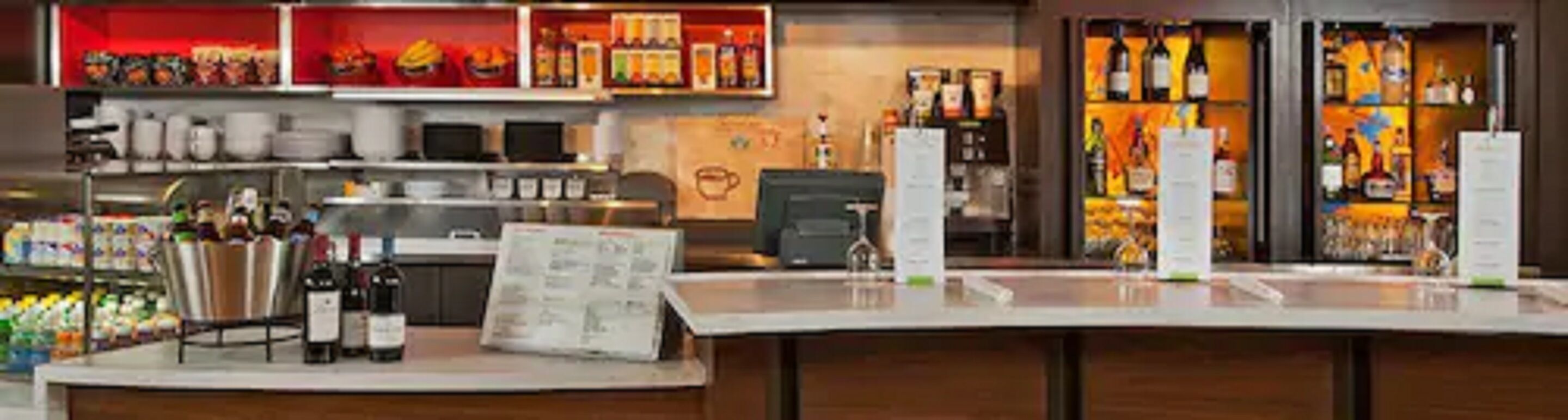 Zona de bar con estantes llenos de botellas, una barra y un atril para el menú.
