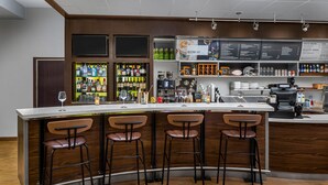Un espace bar doté d’un comptoir incurvé, de quatre tabourets, d’un téléviseur fixé au mur et d’un tableau affichant le menu, placé au-dessus du comptoir.