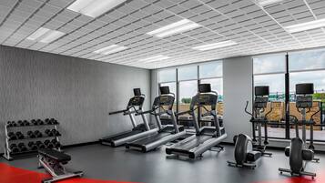 Una palestra con tapis roulant, manubri e macchinari per pesi, ampie finestre e pavimento rosso.