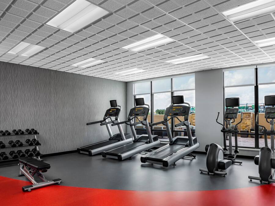 Una palestra con tapis roulant, manubri e macchinari per pesi, ampie finestre e pavimento rosso.