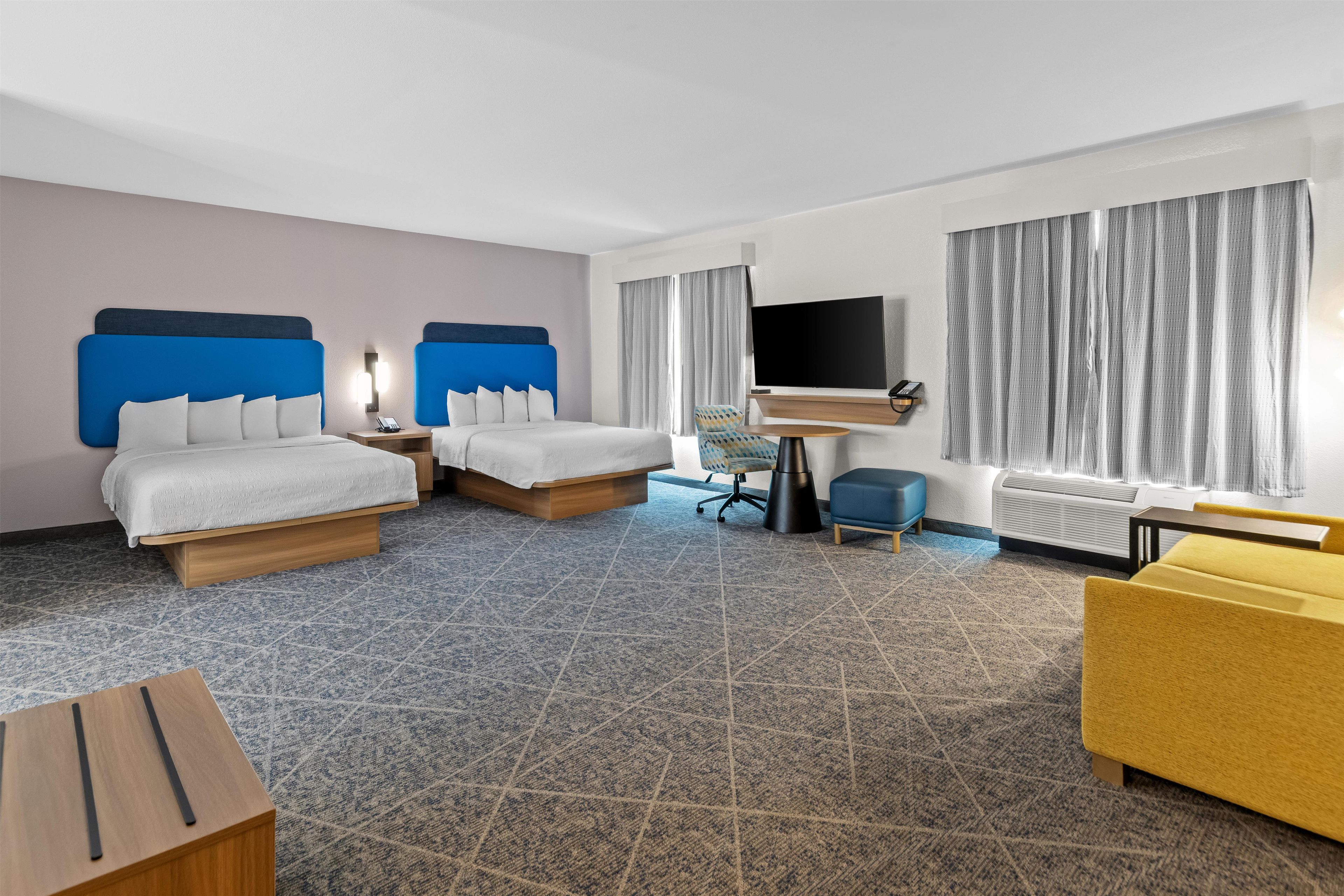 Ein Hotelzimmer mit zwei Betten, einem Schreibtisch mit Stuhl, einem Fernseher und einem Sofa.