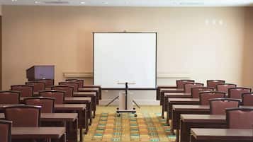 A conference room with rows of tables and chairs, a projection screen, and a carpeted floor.