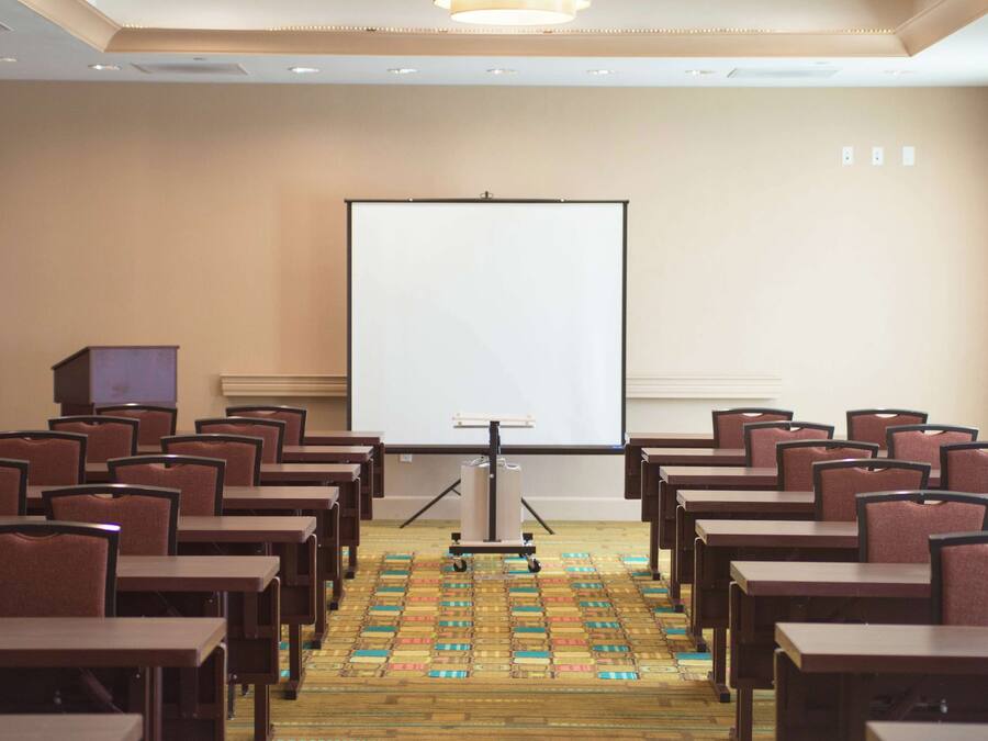 A conference room with rows of tables and chairs, a projection screen, and a carpeted floor.