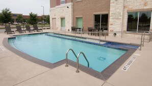 A swimming pool with lounge chairs and tables, a stone building with a sign indicating an emergency phone by the pool gate, and a clear sky. - Hampton Inn & Suites Dallas/Frisco North-FieldhouseUSA (Frisco)