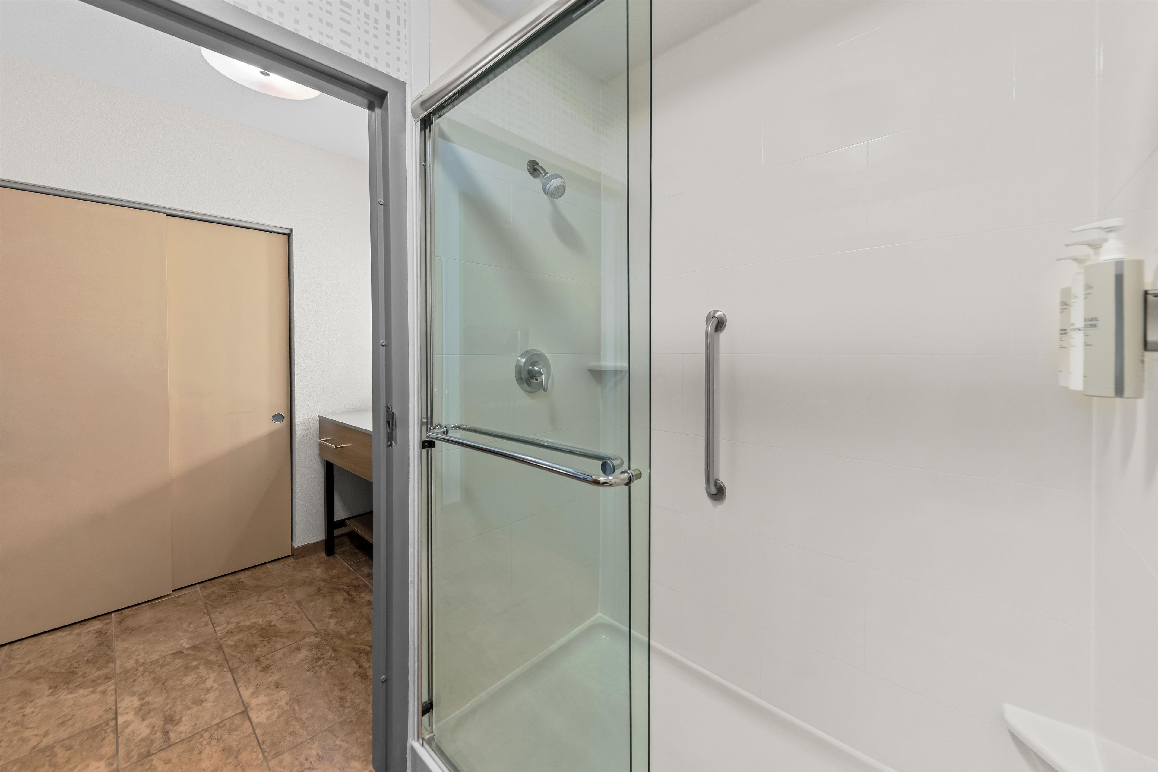 A modern bathroom with a glass shower enclosure, a white sink, and a beige door.