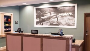 A hotel reception desk with a framed picture of a park bench and the word "explore." - Hampton Inn & Suites Dallas/Frisco North-FieldhouseUSA (Frisco)