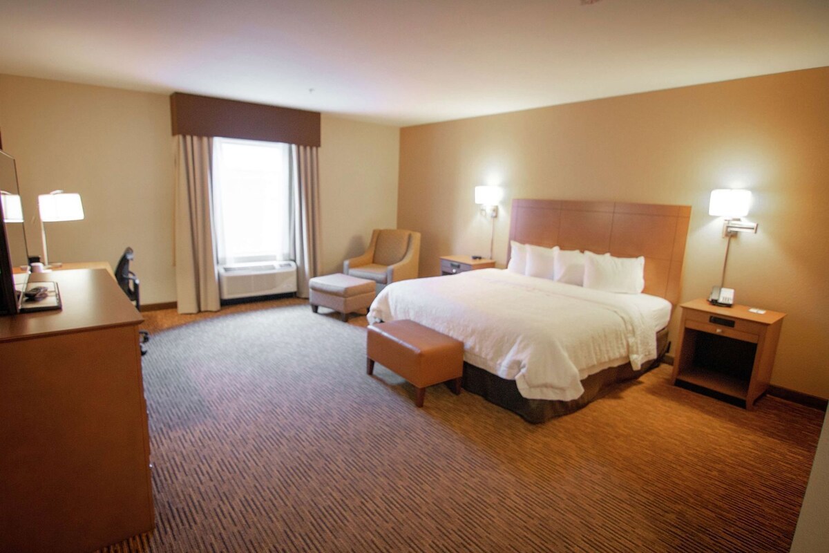 A hotel room with a bed, a desk, a chair, a bedside table, and a lamp.