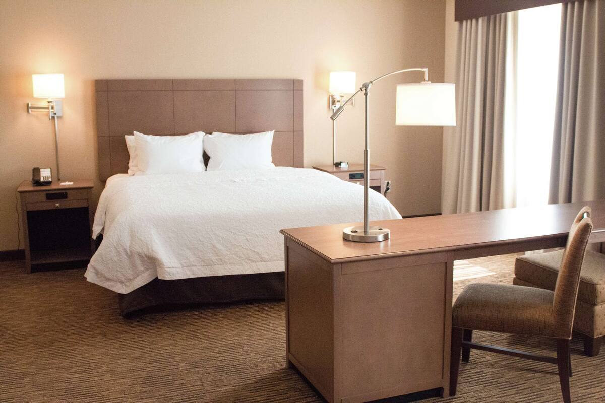 Una habitación de hotel con cama, mesitas de noche, escritorio, silla y lámpara.