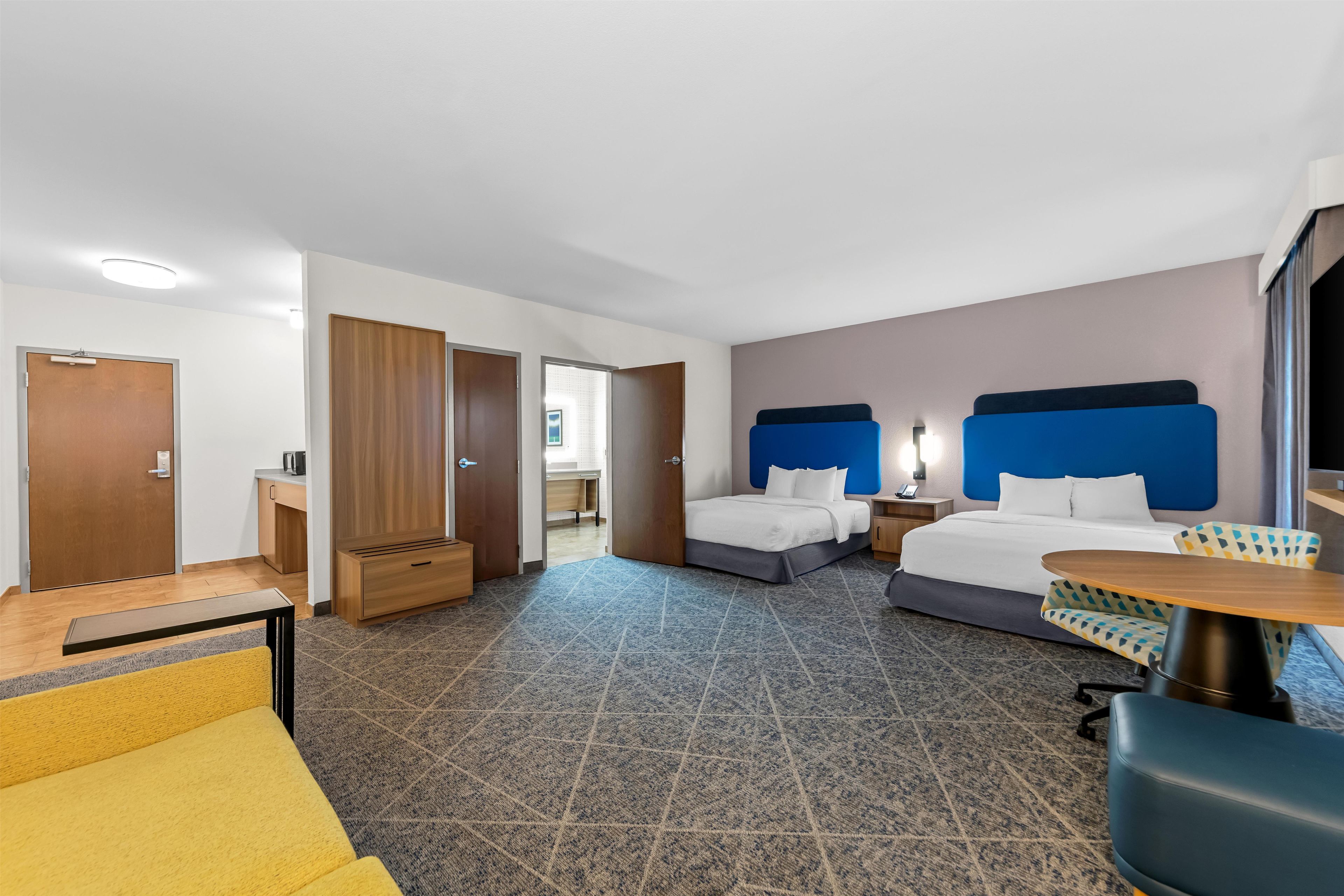 A hotel room with two beds, a desk, a chair, and a small table.