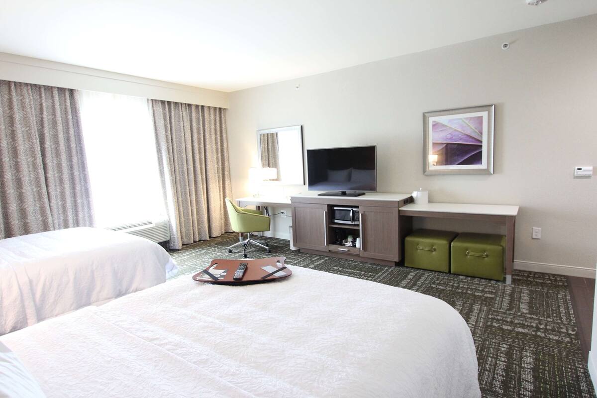 A hotel room with two beds, a desk with a flat-screen TV, a chair, and a small cabinet.